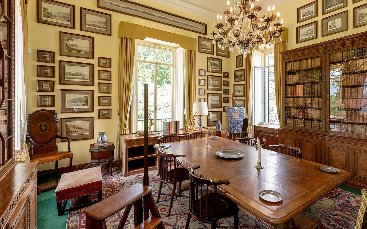 A room of Villa del Balbianello hung with framed antique maps around a long wooden table